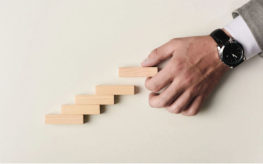A man's hand stacking wooden blocks like stairs.