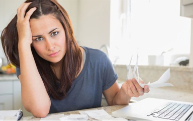 A woman holding receipts in one hand with her other hand on her head.