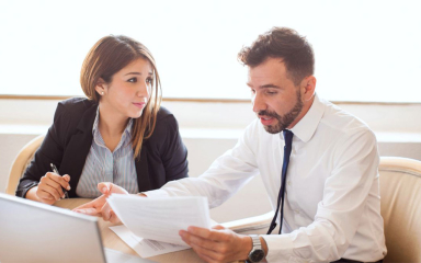 A man and woman at a table with an open laptop and papers.