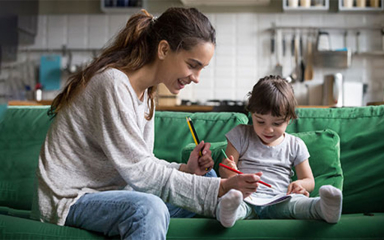 A woman and child sitting on a green couch coloring.