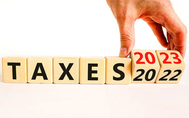 A hand lining up wooden blocks to say Taxes 2023