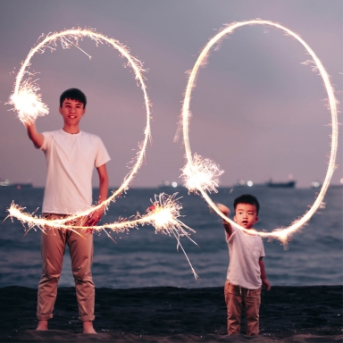 two kids standing on beach spelling out 20 in the air with sparklers