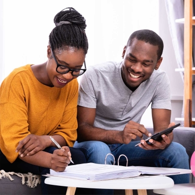 young woman and man sitting, smiling and looking over paperwork with a calculator