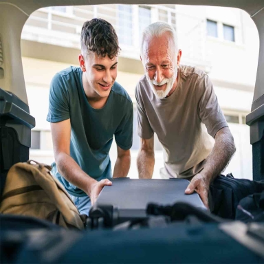 Two men Teenager and senior grandfather pack baggage in trunk of car