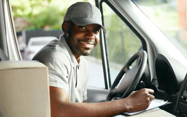 A delivery driver with a box next to him sitting in a truck.