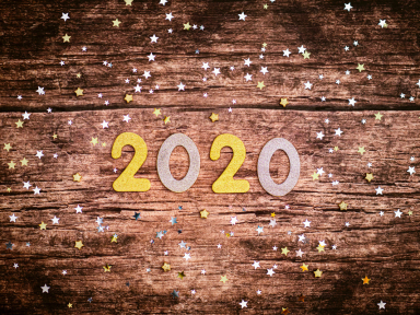 paper cut outs of the number 2020 on a wood background with star shaped confetti