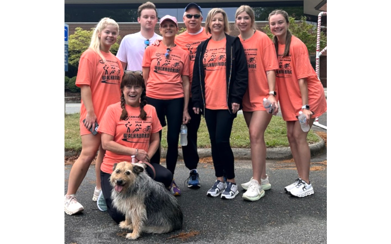 Men, women and a dog all wearing orange shirts, posing for a group photo.