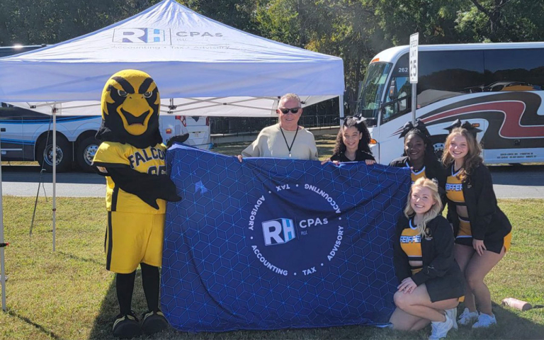A man, mascot and cheerleaders holding a sign.