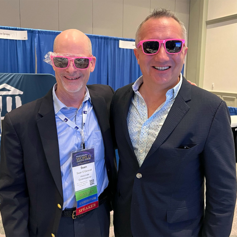 Two men in suits wearing bright pink sunglasses.