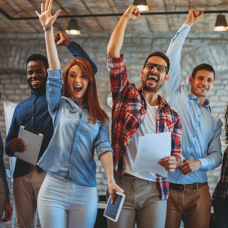 Men and women in an office yelling and pumping their fists.