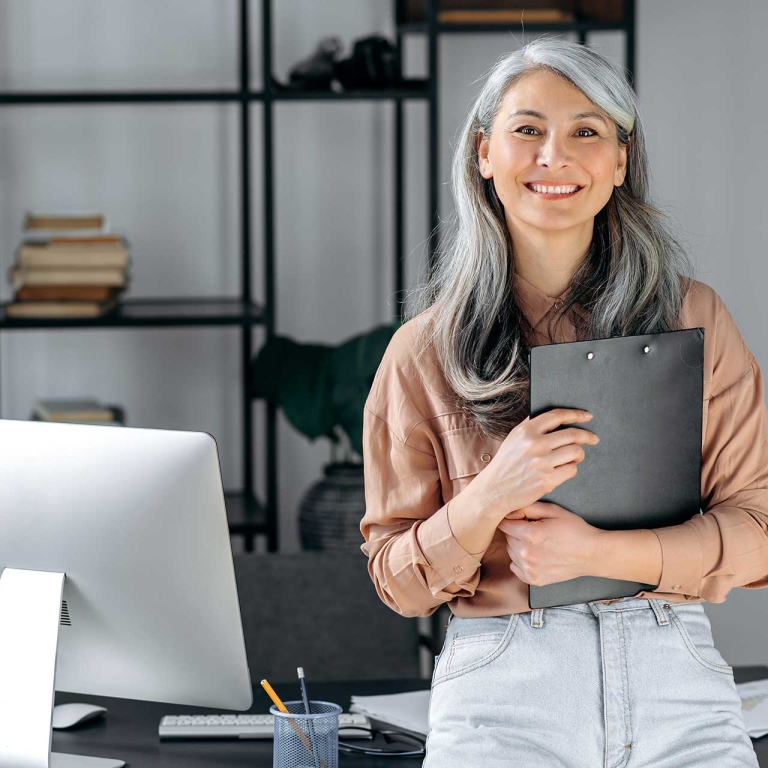 A woman sitting on a desk, holding a clipboard