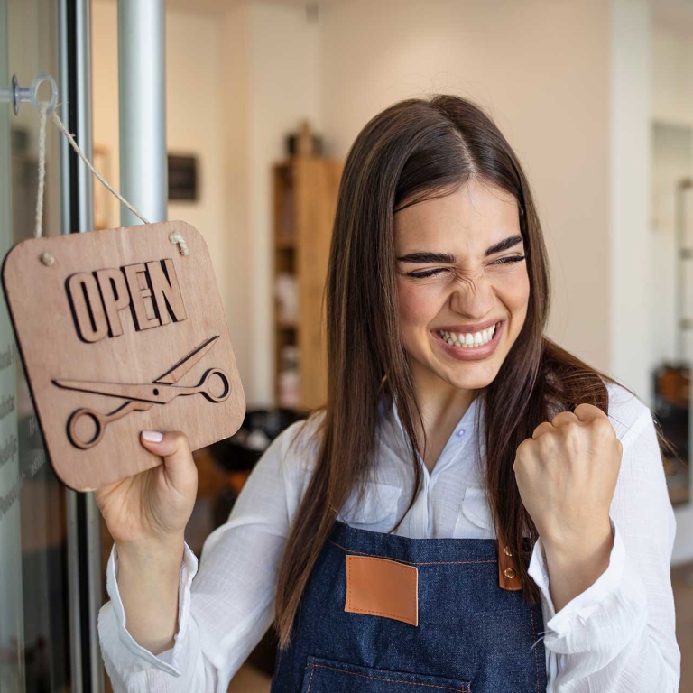 A business woman holding an open sign and smiling while pumping her fist.