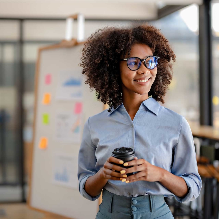 A woman holding coffee and smiling in an office.