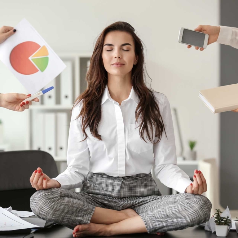 A woman in a meditative pose while people are trying to hand her several work items.