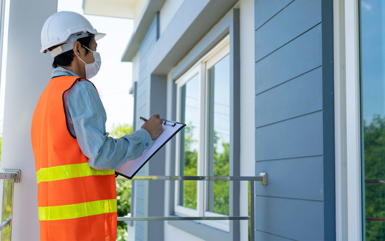 A man with a hardhat and clipboard looking at a home.