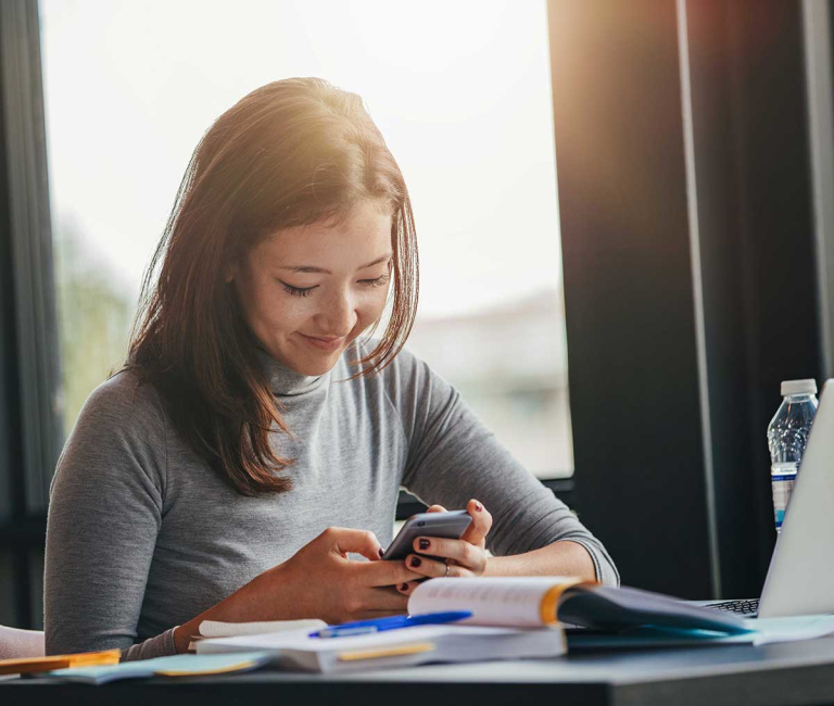 young lady inside at desk looking down at phone