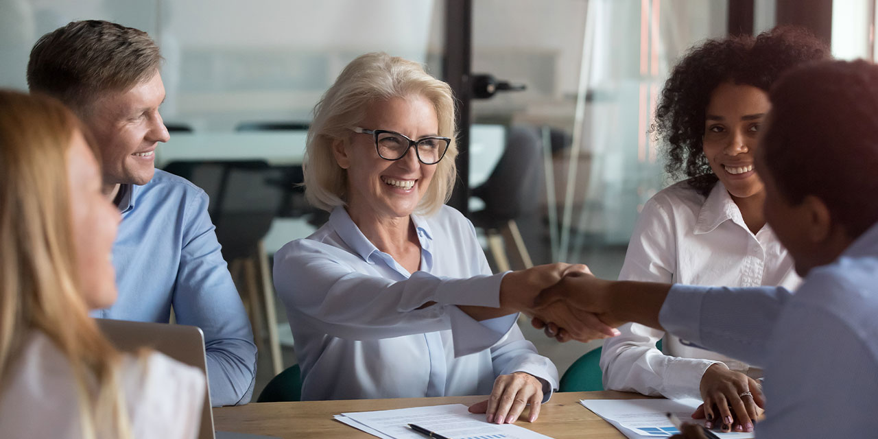 Business professionals at a table and a man and woman shaking hands.
