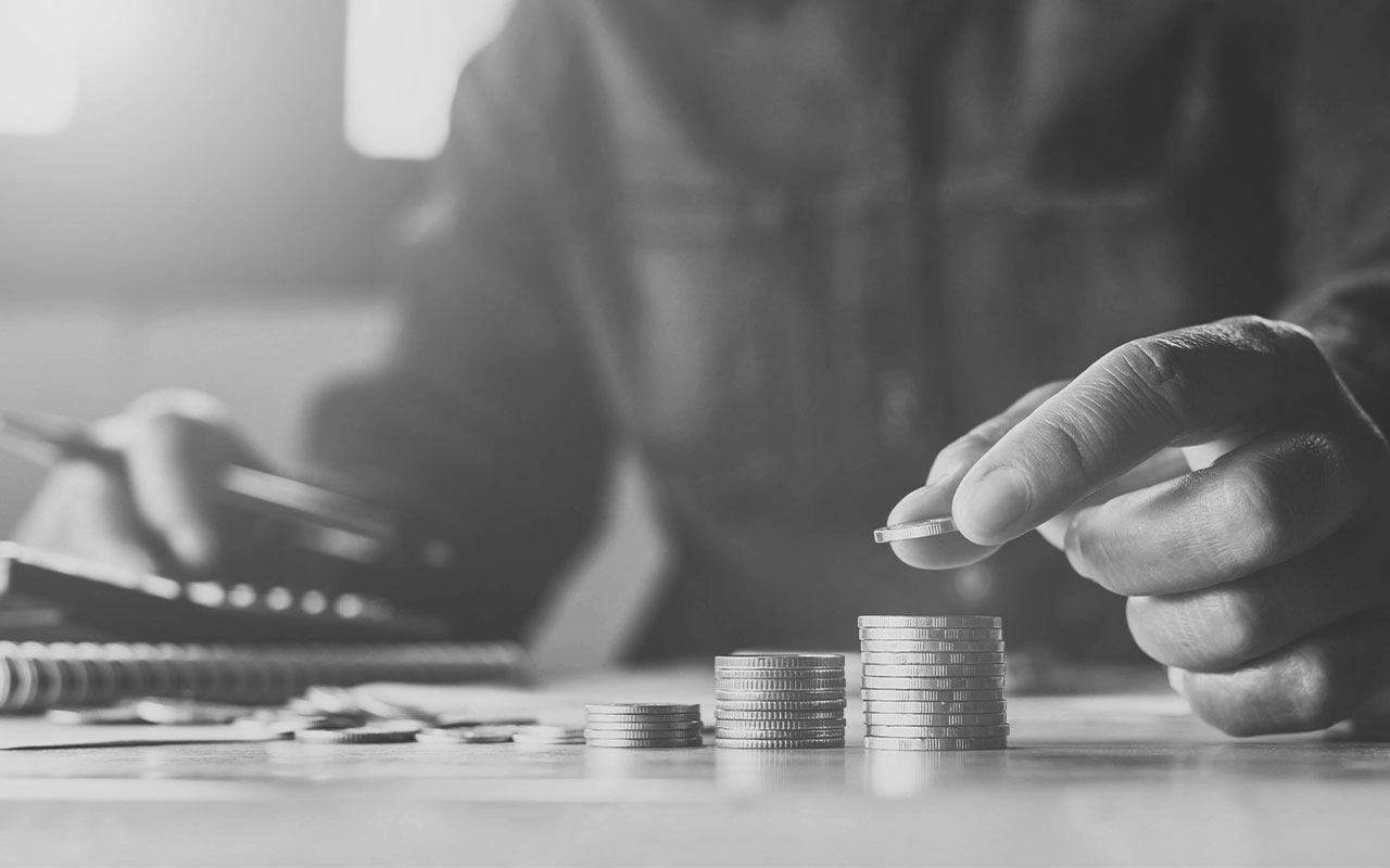 A person holding a pen, using a calculator while counting coins.