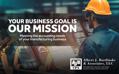 A man wearing a hardhat and safety goggles looking at a large digital screen.