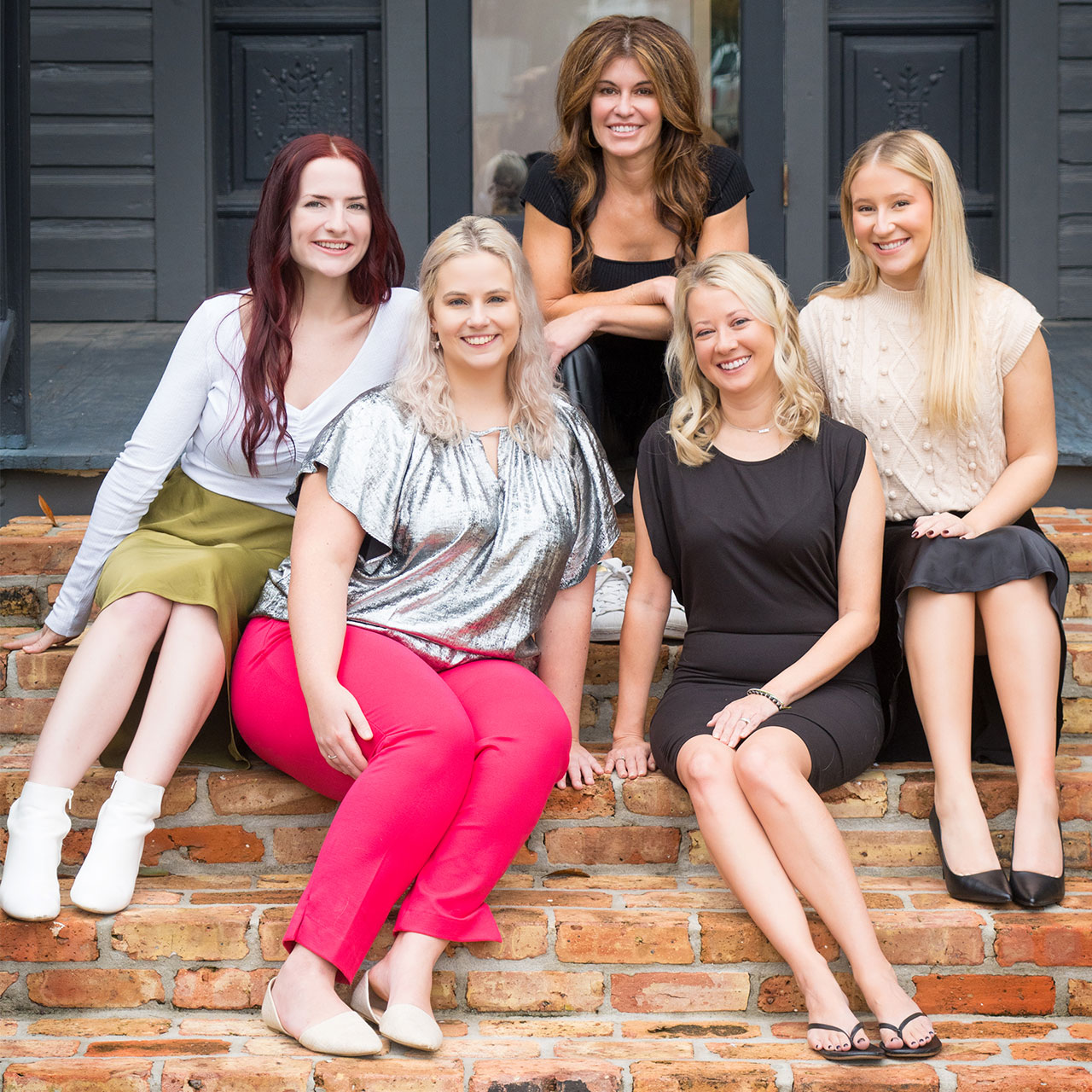 Female business professionals, posing for a photo, sitting on steps.