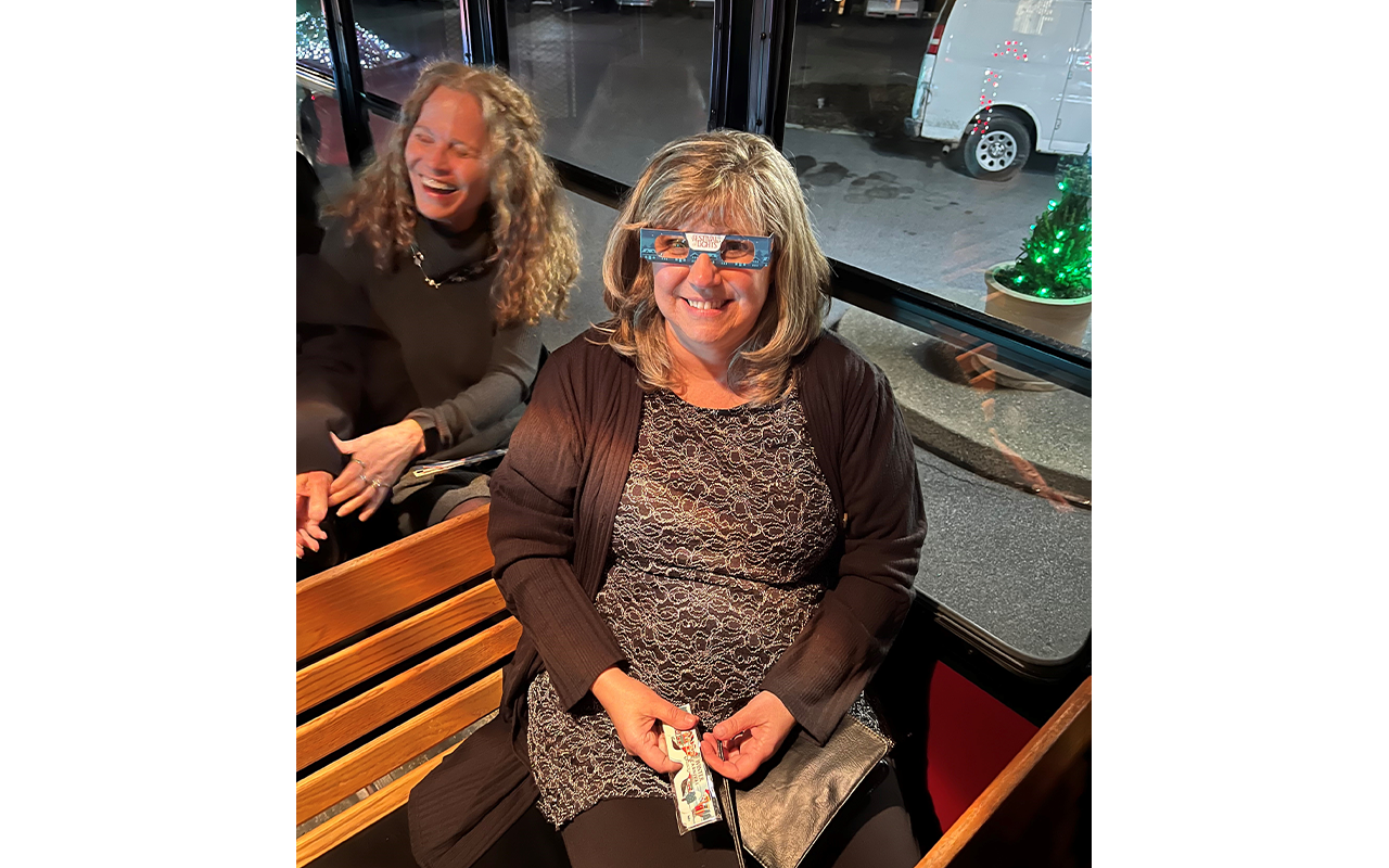 Two women on a trolly ride. One of them is wearing Festive Lights glasses.