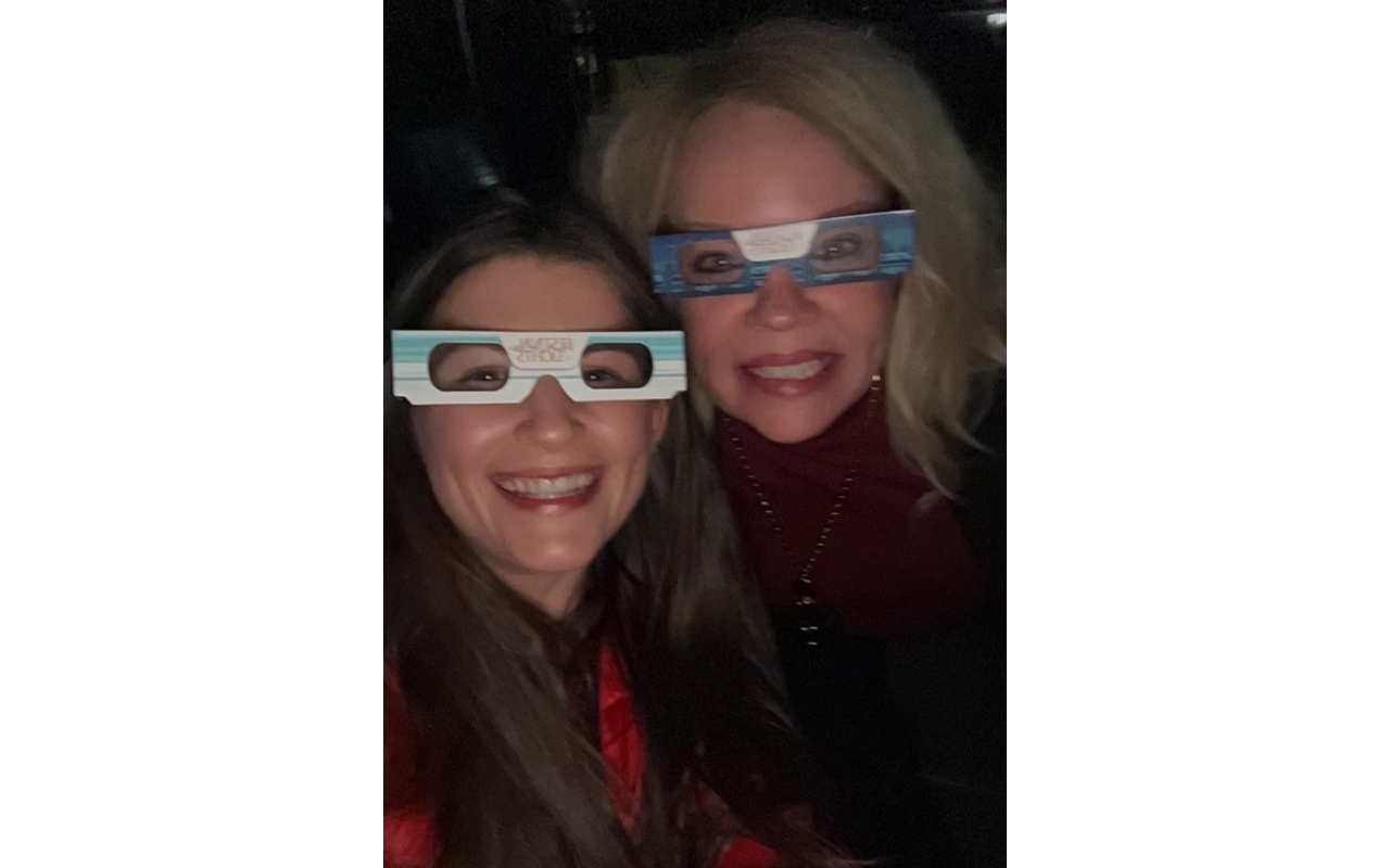 Two women wearing paper glasses, posing for a selfie.