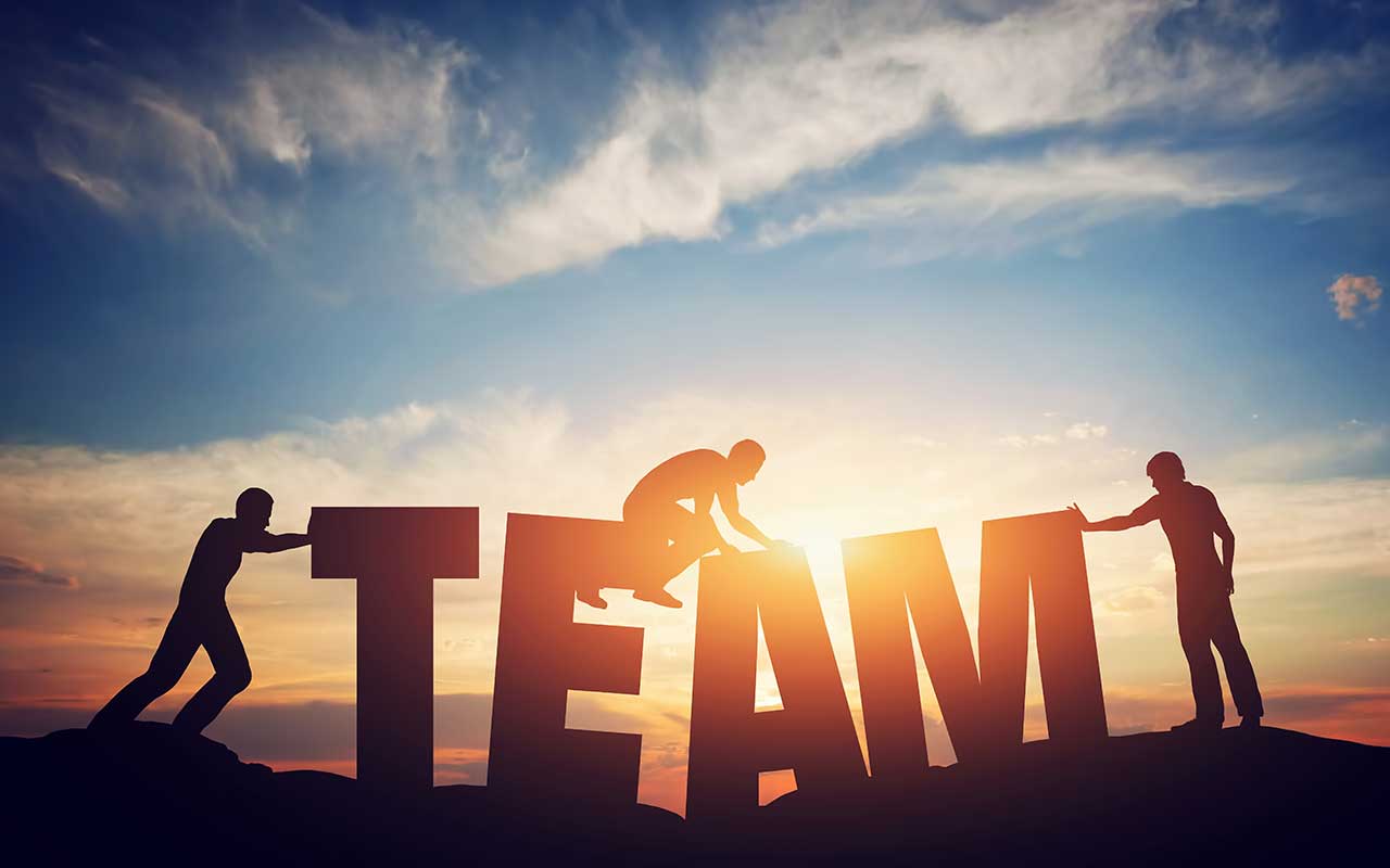 People holding up the word team while the sun is setting in the background.