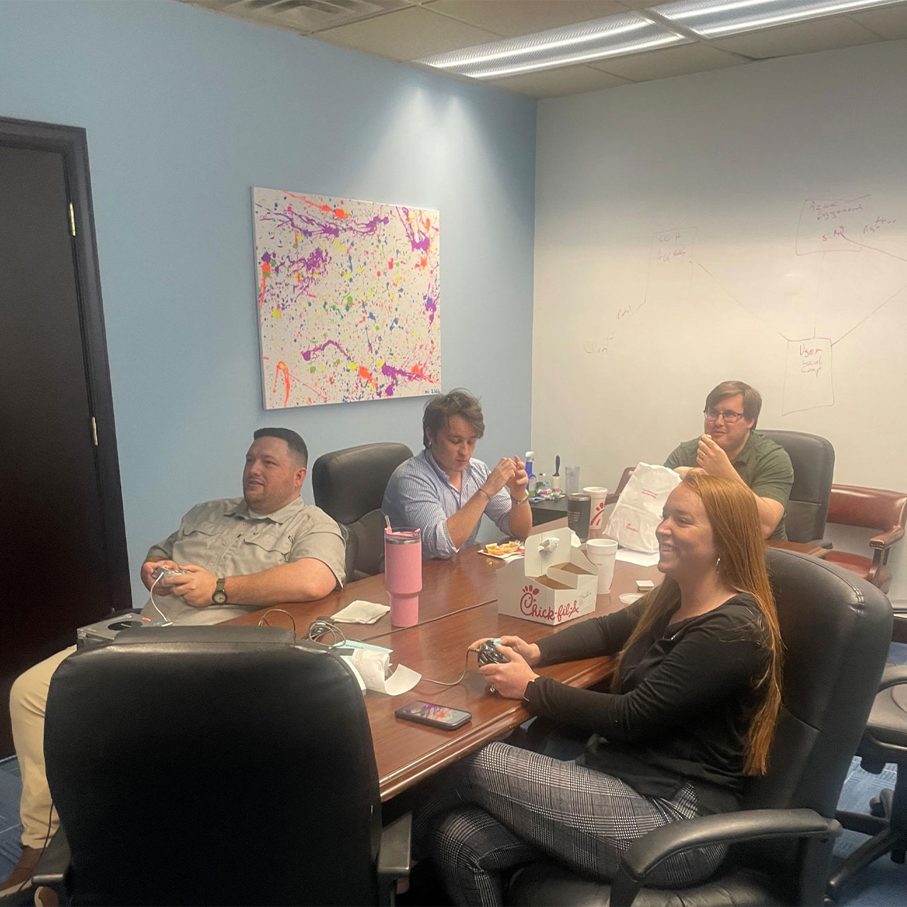 A group of people sitting around a conference table playing video games and eating fast food.