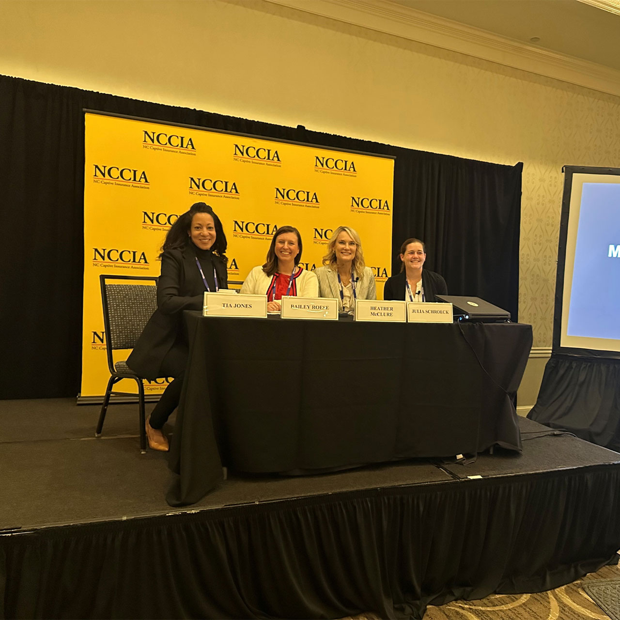Business professionals at a table on a stage at a conference.