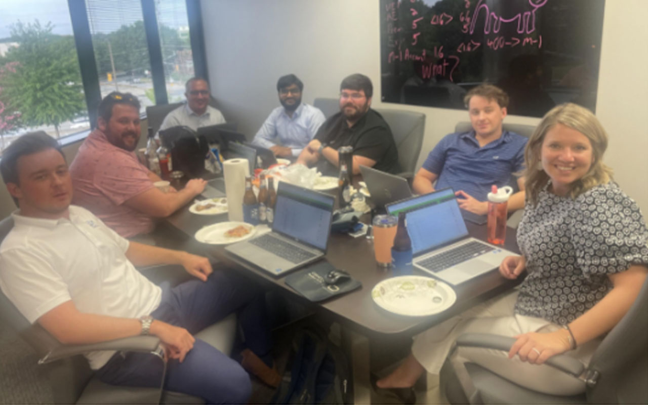 A group of people with their laptops and food gathered around a meeting table.
