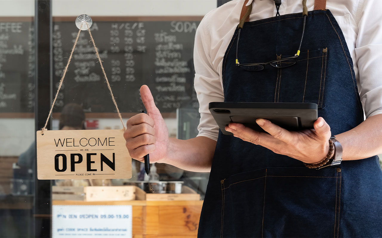 Person holding a tablet standing in front of an open sign.