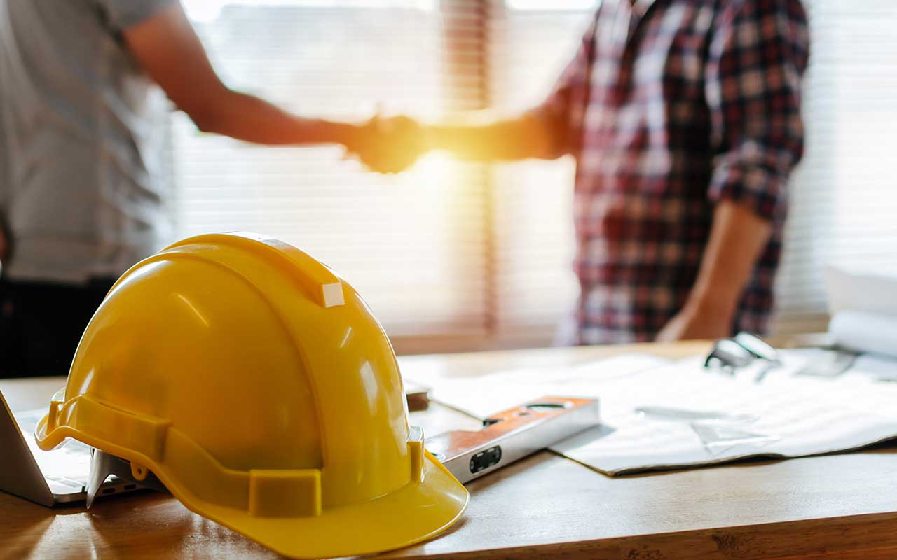 yellow construction helmet in foreground with two people shaking hands in background