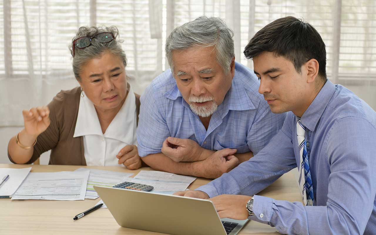 Three people at a desk reviewing documents and looking at a laptop.