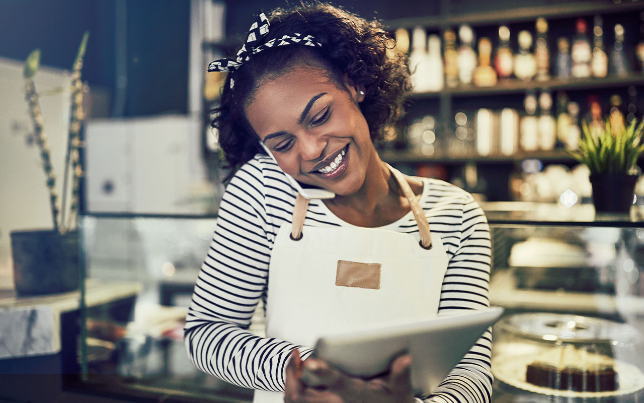 Woman in a bakery holding a tablet while talking on the phone.