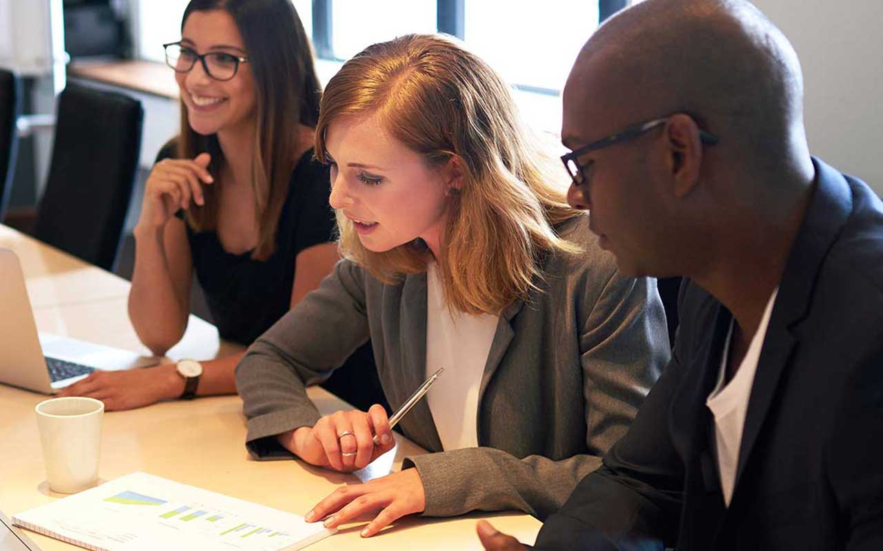 Three professionals gathered around a table looking at paperwork