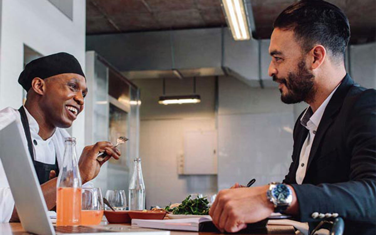 A restaurant worker and man sitting at a table, laughing