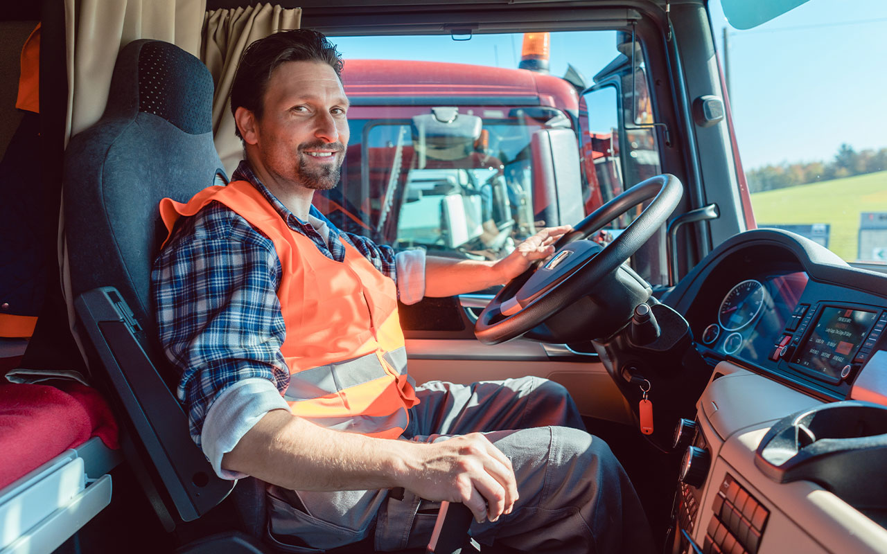 Man wearing an orange vest driving a semi truck.