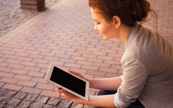 young female sitting and reading content on a tablet outside