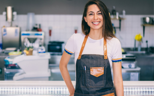 A woman wearing an apron smiling in a bakery kitchen.