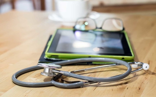 Stethoscope, a tablet, glasses and a coffee cup and saucer on a table.