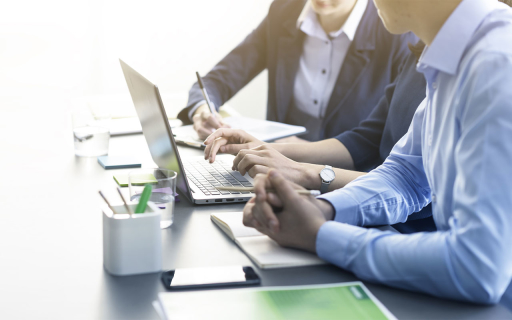 Three people at a desk working at a laptop.