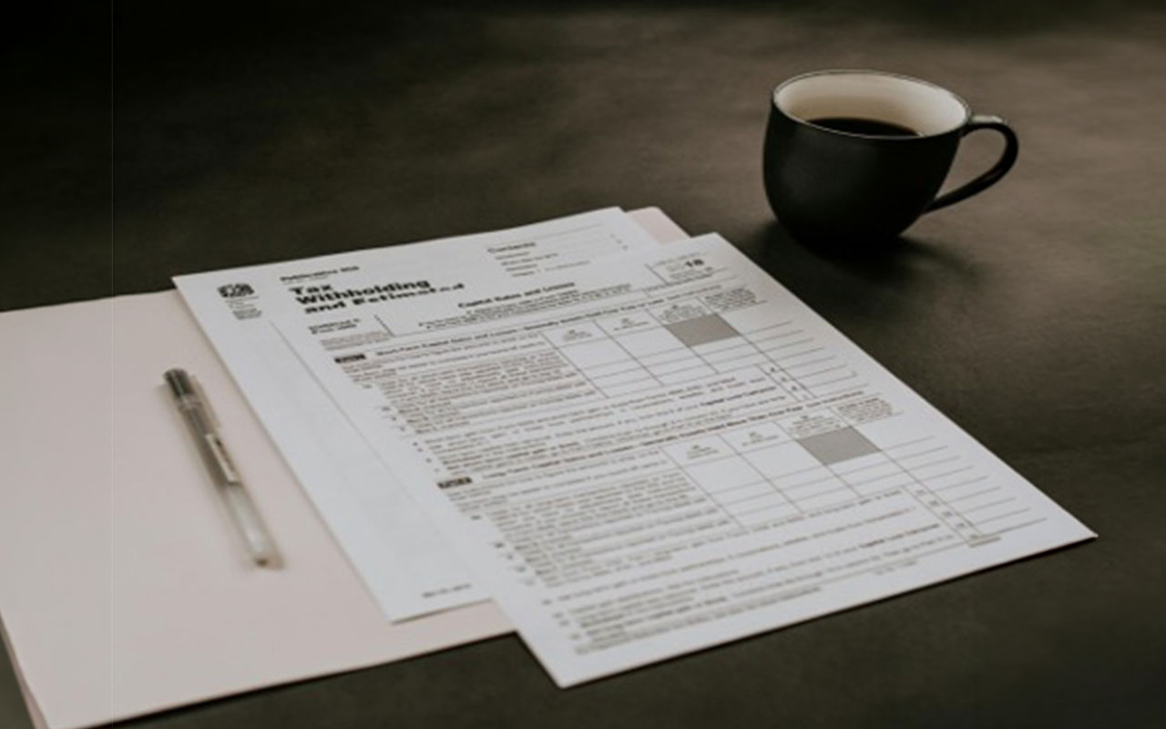 Papers, a folder, a pen, and a cup of coffee on a table.