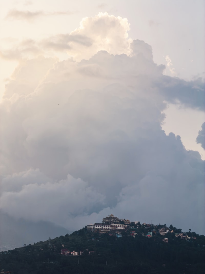 A hill topped with a monastery complex under massive dramatic cloud formations in Lalitpur, Nepal