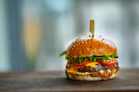 Saftiger Cheeseburger mit frischem Salat und Tomaten auf einem Holztisch