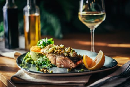 Gebratenes Lachsfilet mit Gemüse und Zitrone, serviert mit einem Glas Riesling Weißwein