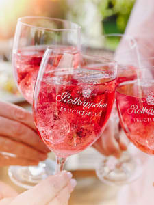 Menschen stoßen mit Gläsern Rotkäppchen-Fruchtsecco-Granatapfel an.