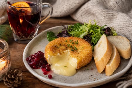 Gebackener Camembert mit Preiselbeeren, Baguette und Salat neben einem Glas roter Glühwein
