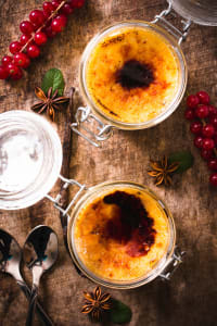 Crème Brûlée mit knuspriger Karamellkruste in Gläsern, serviert mit Johannisbeeren, Sternanis und Vanille auf einem rustikalen Holztisch.