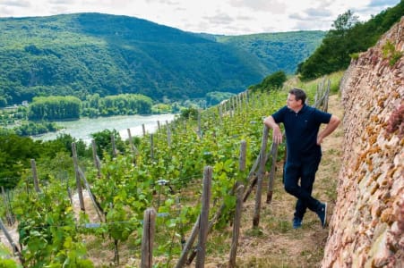 Johannes Leitz steht im Weinberg mit Rebstöcken am Rheinufer.