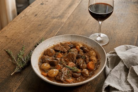 Geschmortes Lammragout mit kleinen Kartoffeln, Karotten und mediterranen Kräutern, serviert mit einem Glas Mandrarossa Nero d'Avola als passende Speisebegleitung.